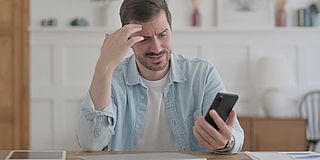 Beleidigungen im Internet Mann blickt nachdenklich auf sein Smartphone